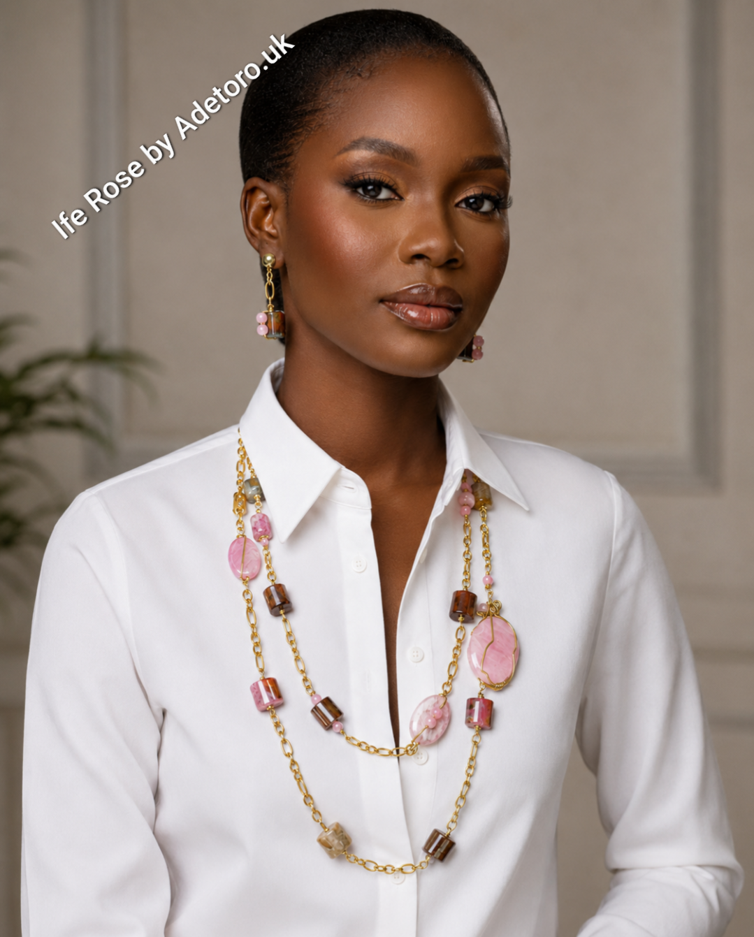 A woman wearing a white collared shirt models a multi-strand necklace and matching drop earrings. The jewelry features gold-tone chains and links accented with pink stone beads, brown cylindrical beads, and small gold charms.