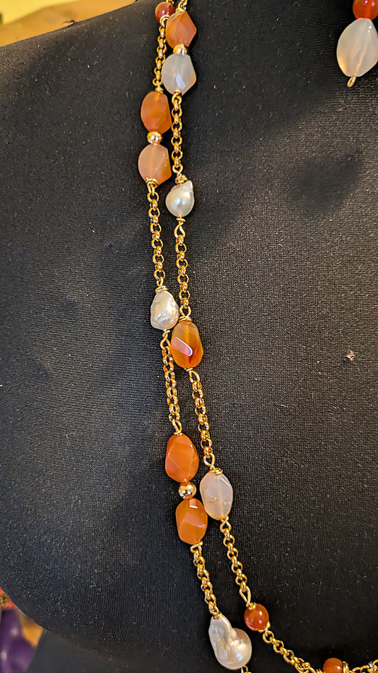 A gold chain necklace with irregular orange agate stones and white baroque pearls, displayed on a black mannequin bust.